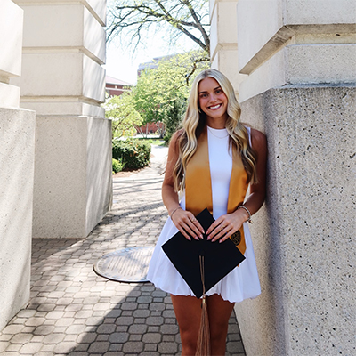 Amira Garwood stands in front of the Engineering Fountain holding her graduation cap.