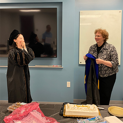 Yitong Wang stands in a cap and gown with her hands covering her mouth next to Karen Foli.