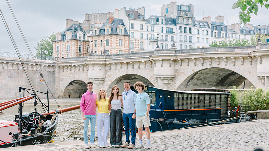 The Baker family stands in front of a bridge over a canal with buildings in the background